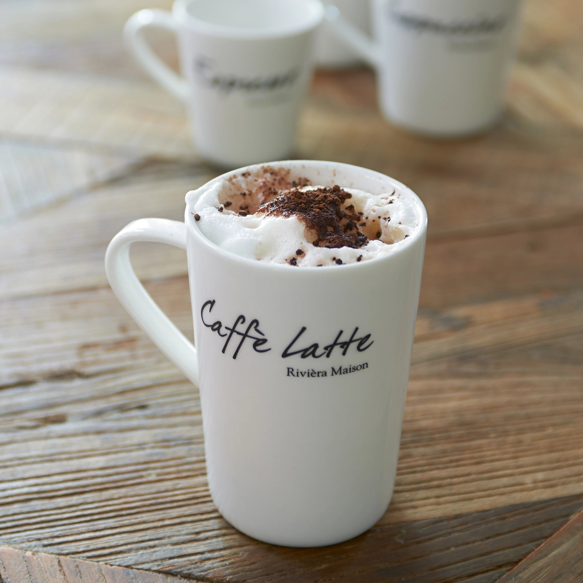 Weiße Caffè Latte Tasse aus Porzellan von Riviera Maison mit schwarzer Caffè Latte-Aufschrift.