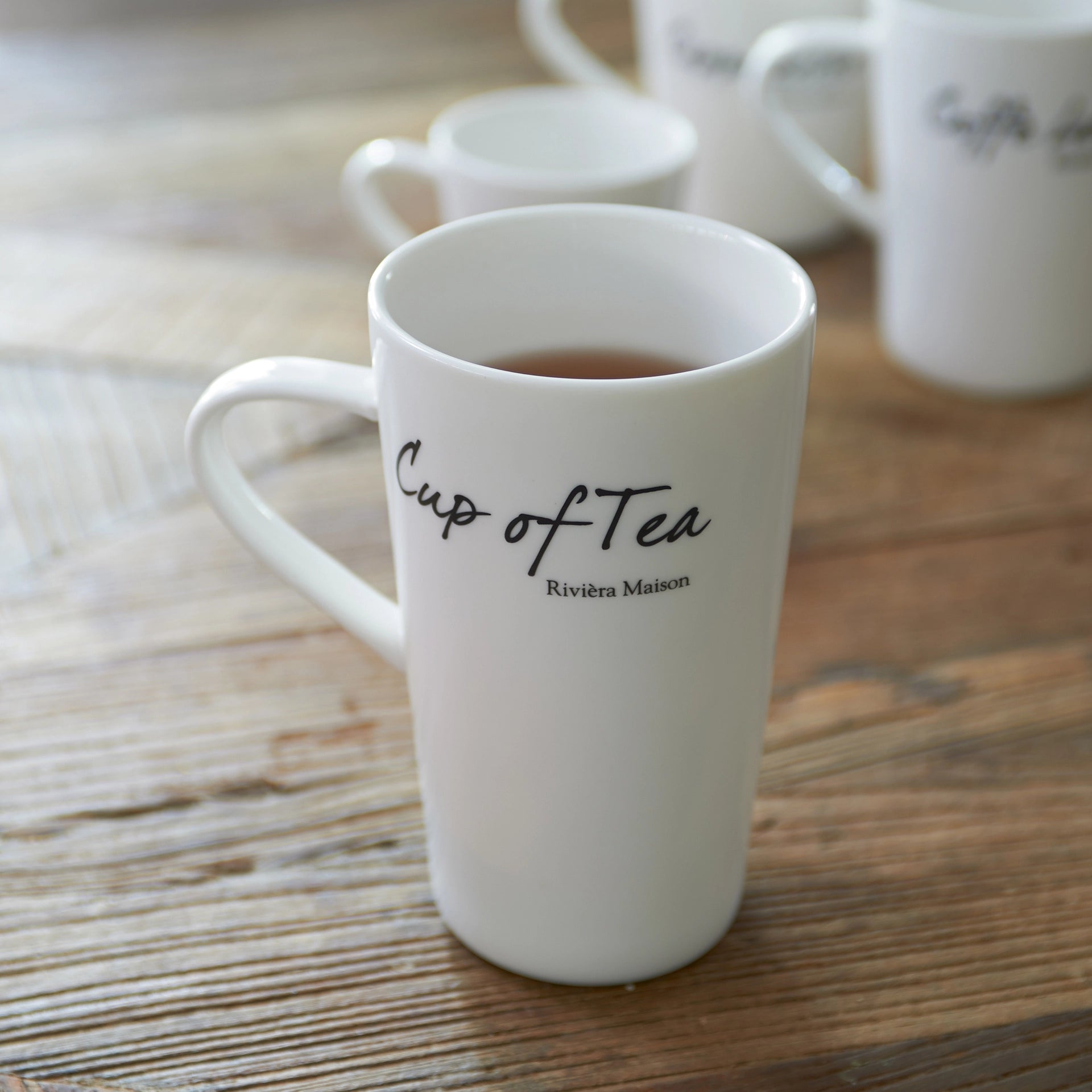 Weiße Teetasse aus Porzellan von Riviera Maison mit schwarzer „Cup of Tea“-Aufschrift.
