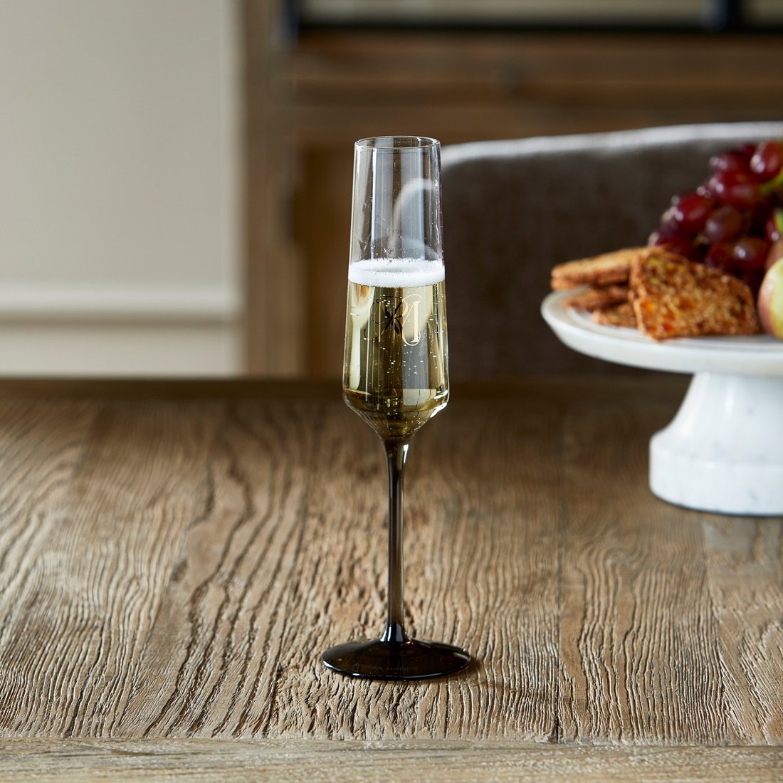 Riviera Maison RM Aura Champagne Glass mit schwarzem Stiel und RM-Monogramm, gefüllt mit Champagner.