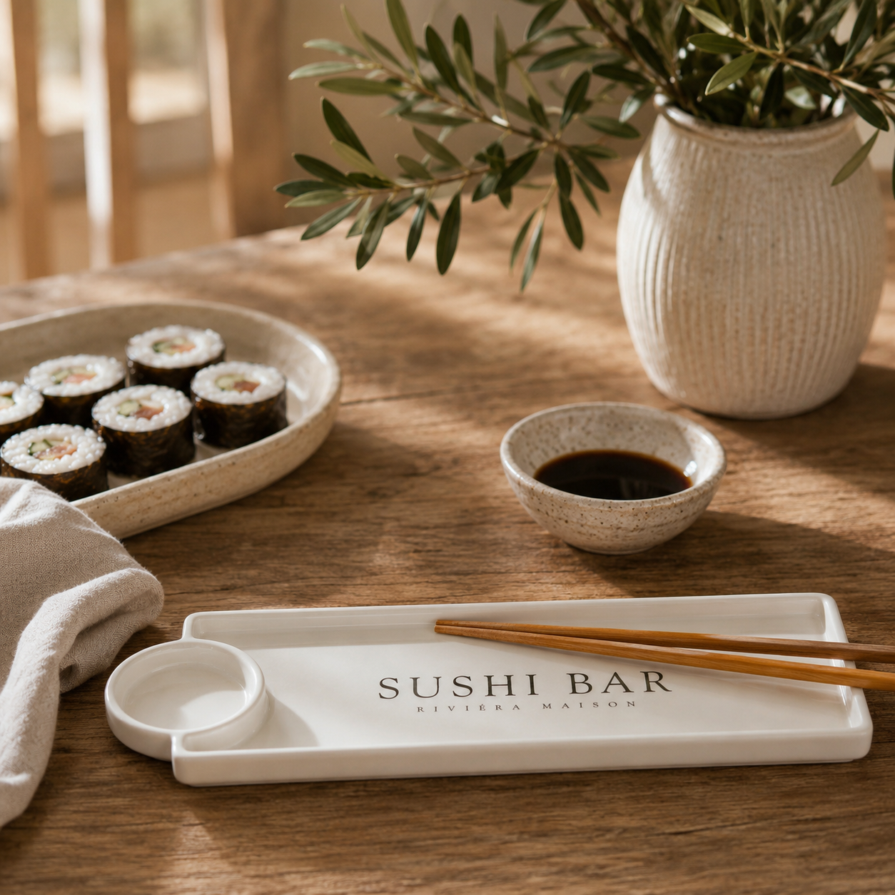 Riviera Maison Sushi Bar Plate aus weißer Keramik mit integrierter Sojasaucenschale und Essstäbchen auf einem rustikalen Holztisch.
