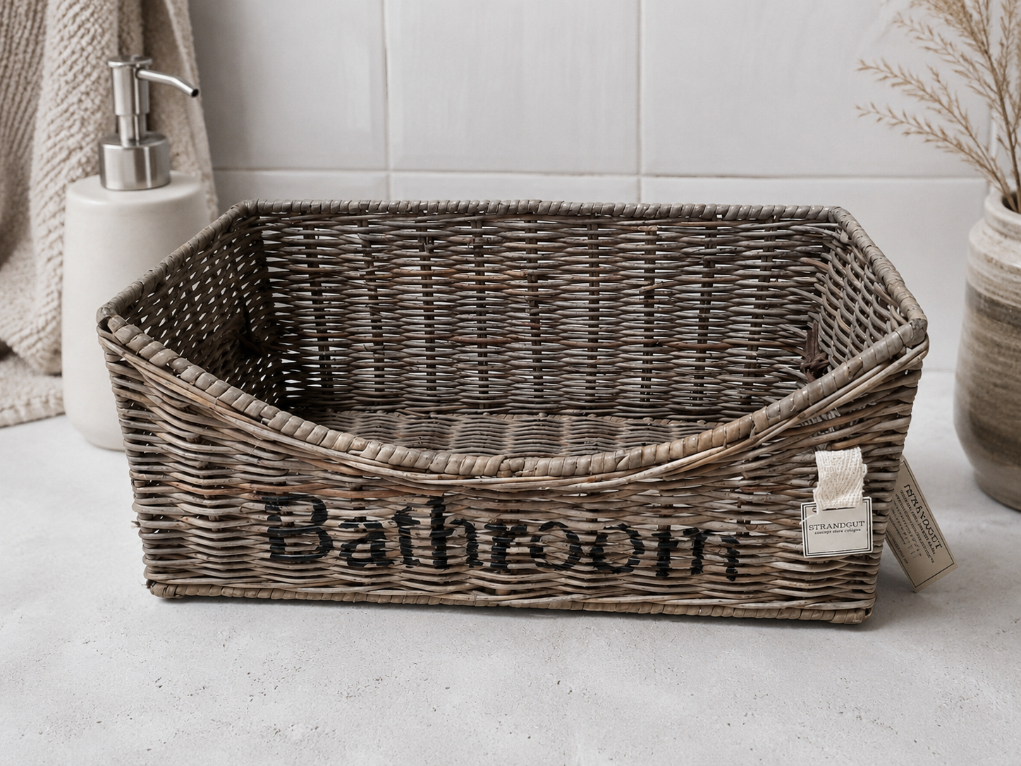 Rattan-Aufbewahrungskorb „Bathroom“ mit eingerollten Handtüchern und Badebürsten als stilvolle Badezimmerorganisation im natürlichen Landhaus- und Beachhouse-Stil.