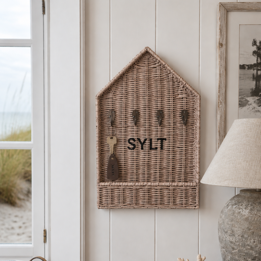 Handgefertigter Rattan Schlüsselkasten mit SYLT-Aufschrift und Schlüssel an Metallhaken im hellen Strandhaus im Coastal-Style.