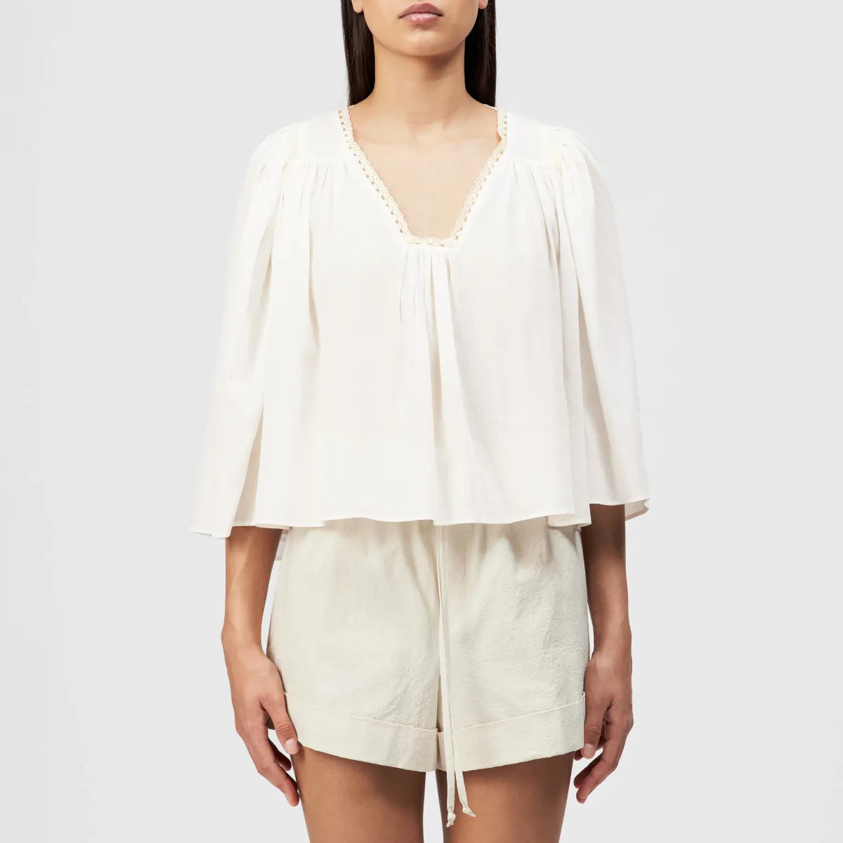 Drykorn Tunika-Bluse ISMARA in Cremeweiß mit weitem Ärmel, Spitzenborte am Ausschnitt und fließender A-Linien-Silhouette. Feminine Sommerbluse aus Baumwoll-Viskose-Mix mit leichter Crêpe-Struktur.