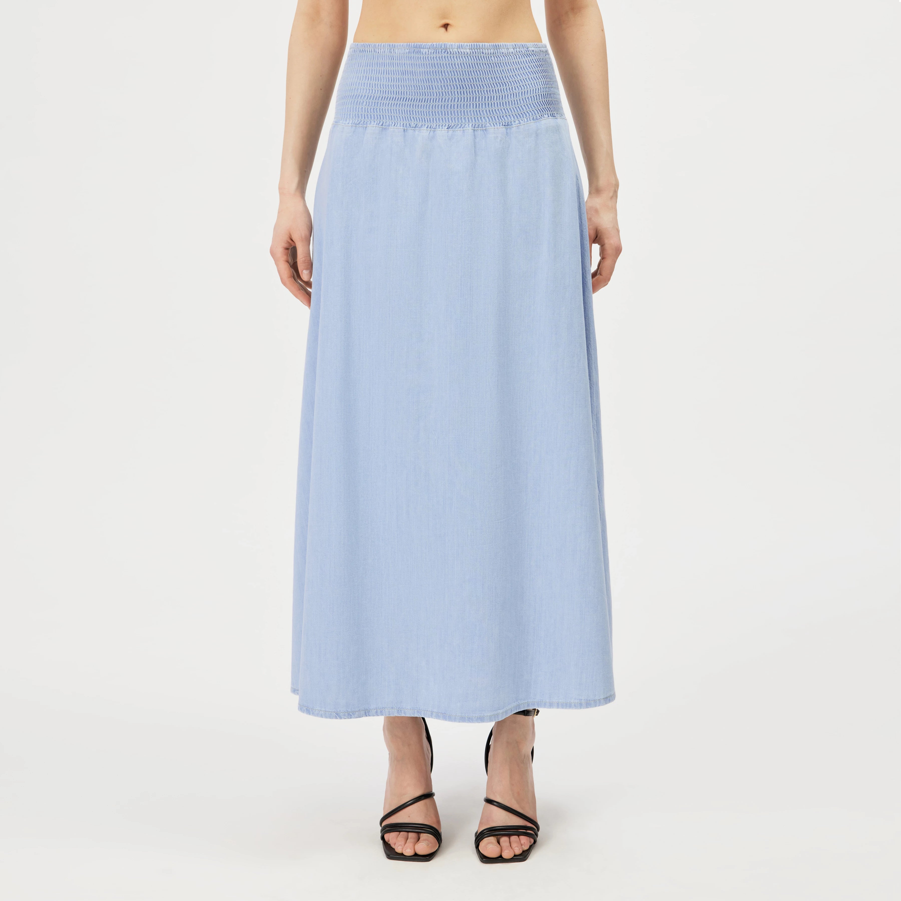 Drykorn Midirock NORIEL aus hell gewaschenem Baumwoll-Denim mit gesmoktem High-Waist-Bund und fließender A-Linien-Silhouette. Knöchellanger Jeansrock im femininen Boho-Stil.