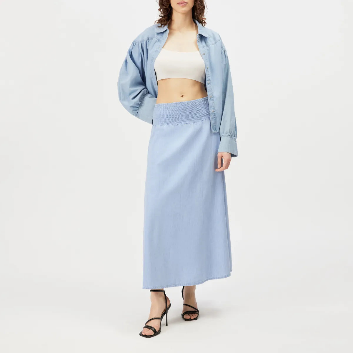 Drykorn Midirock NORIEL aus hell gewaschenem Baumwoll-Denim mit gesmoktem High-Waist-Bund und fließender A-Linien-Silhouette. Knöchellanger Jeansrock im femininen Boho-Stil.