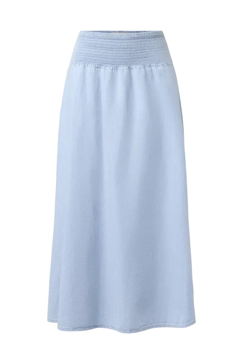 Drykorn Midirock NORIEL aus hell gewaschenem Baumwoll-Denim mit gesmoktem High-Waist-Bund und fließender A-Linien-Silhouette. Knöchellanger Jeansrock im femininen Boho-Stil.