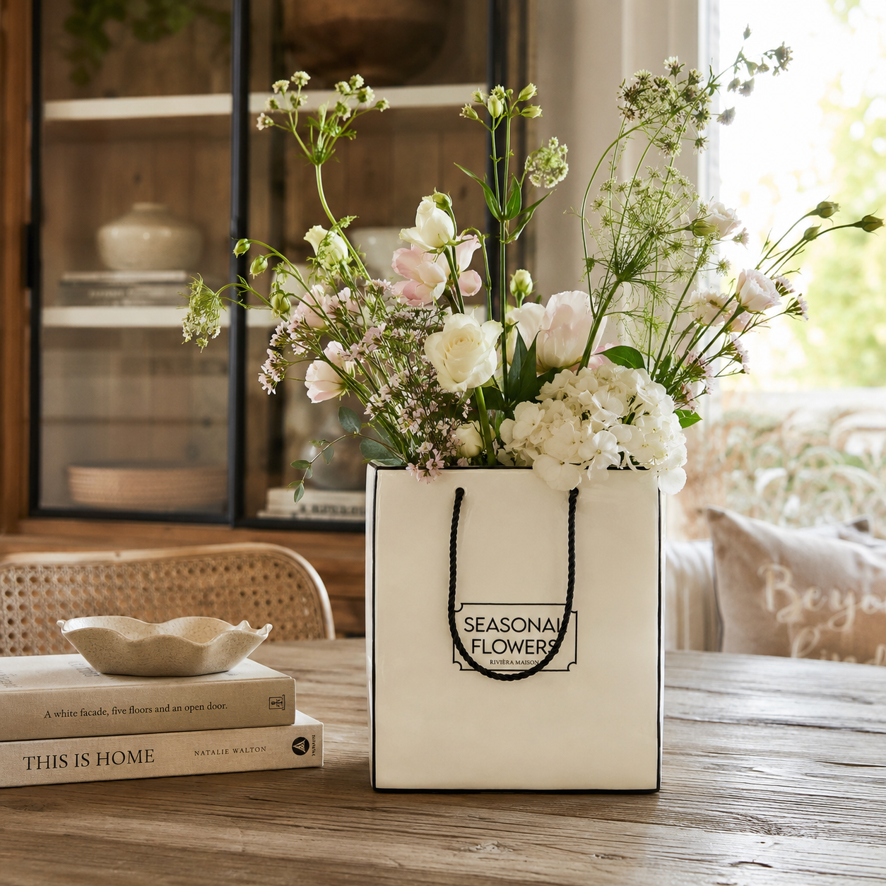 Riviera Maison Seasonal Flowers Vase aus weißer Keramik im Design einer Einkaufstasche mit schwarzen Kordelgriffen.