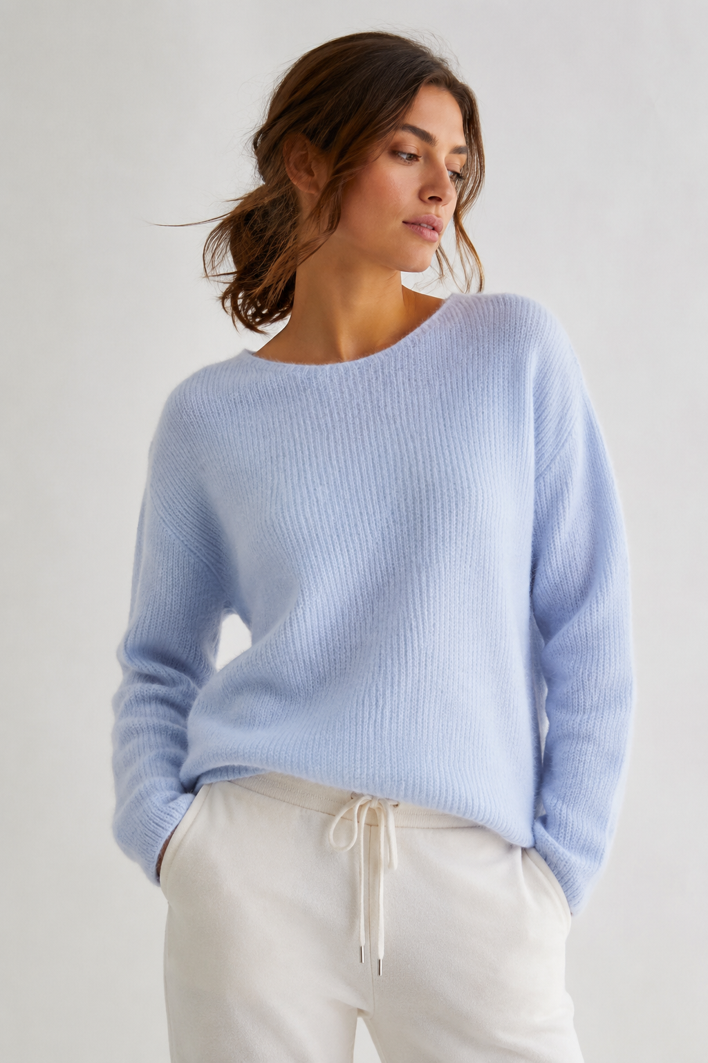 Model trägt den hellblauen DRYKORN IMENY Strickpullover aus weicher Alpaka-Wollmischung mit lockerem Schnitt und Rundhalsausschnitt.