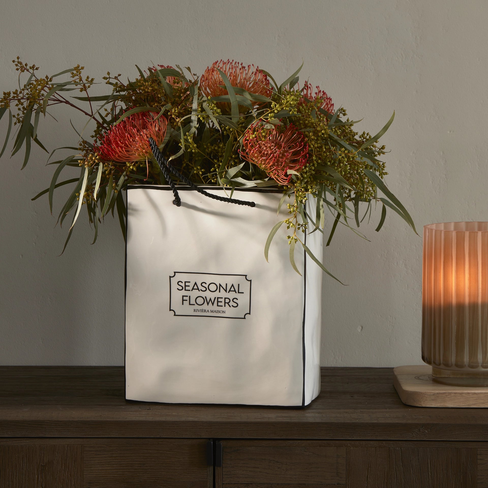 Riviera Maison Seasonal Flowers Vase aus weißer Keramik im Design einer Einkaufstasche mit schwarzen Kordelgriffen.
