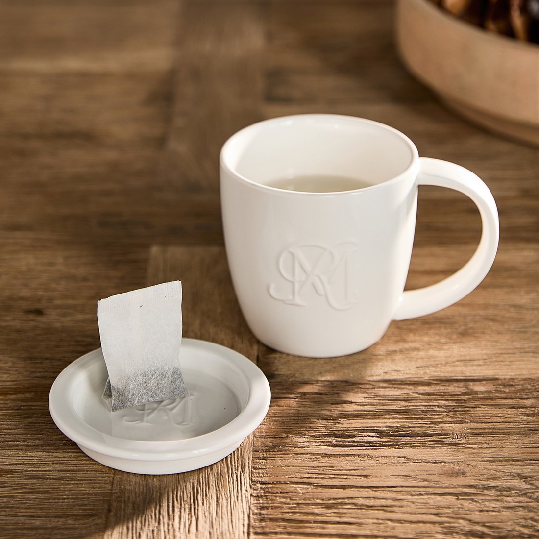 Riviera Maison RM Mug with Tea Tip aus weißer Keramik mit passender Teebeutel-Ablage auf einem rustikalen Holztisch.