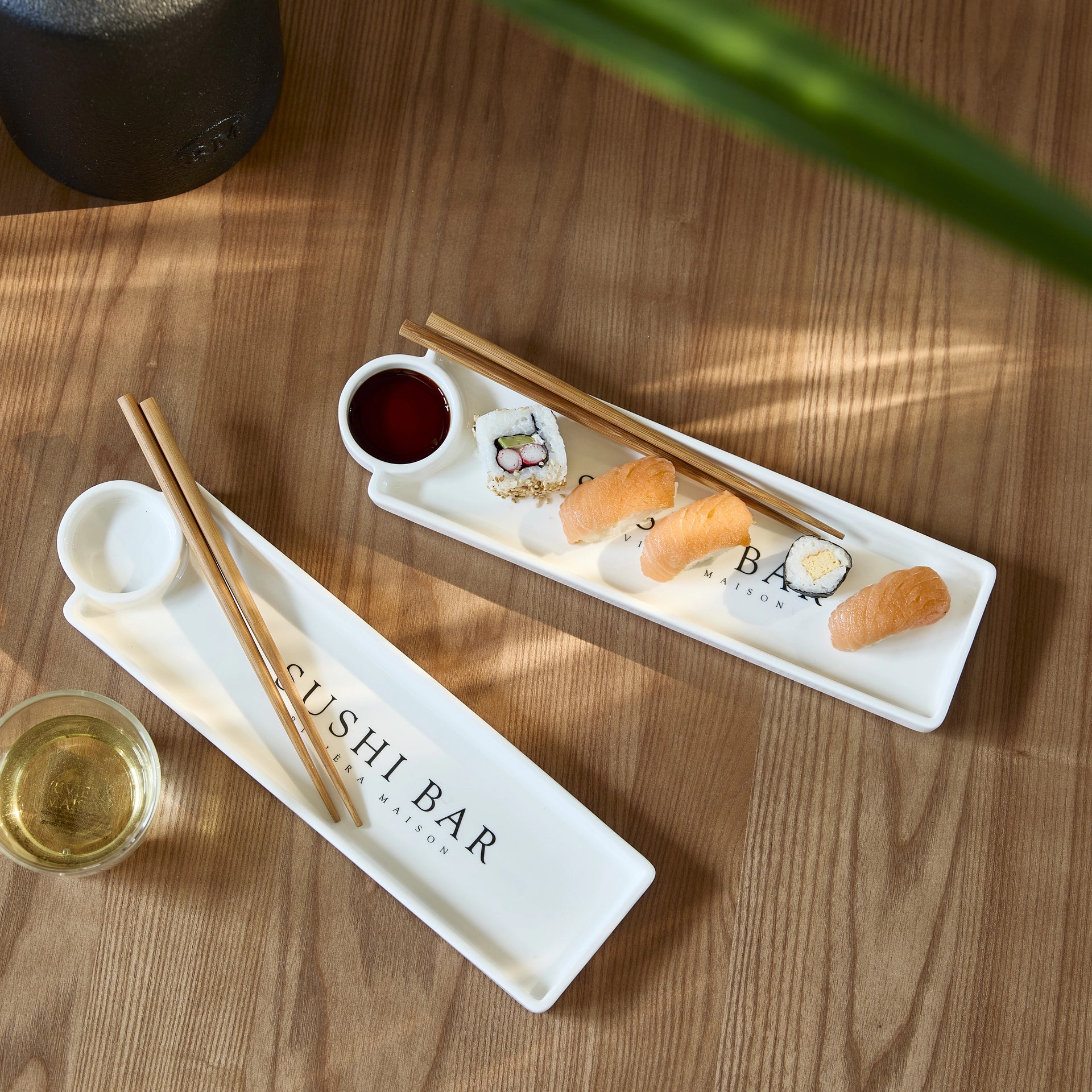 Riviera Maison Sushi Bar Plate aus weißer Keramik mit integrierter Sojasaucenschale und Essstäbchen auf einem rustikalen Holztisch.