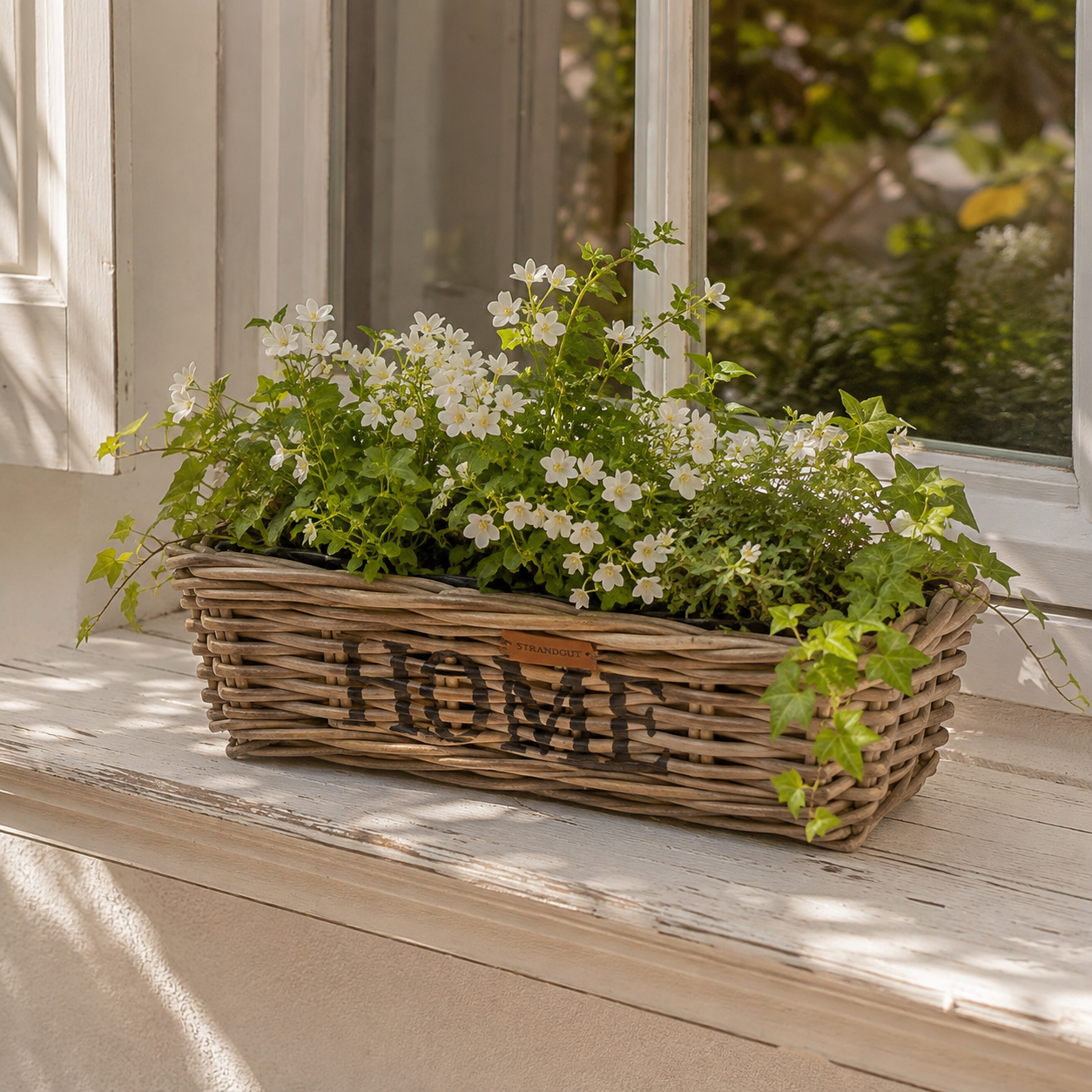 Rattan Planter HOME Größe S mit weißen Blumen und Grünpflanzen auf einer Fensterbank im Landhausstil